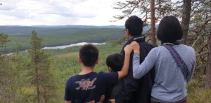 En man, kvinna och två barn tittar ut över en vacker vy från ett berg. Familjen är vänd med ryggen mot kameran,